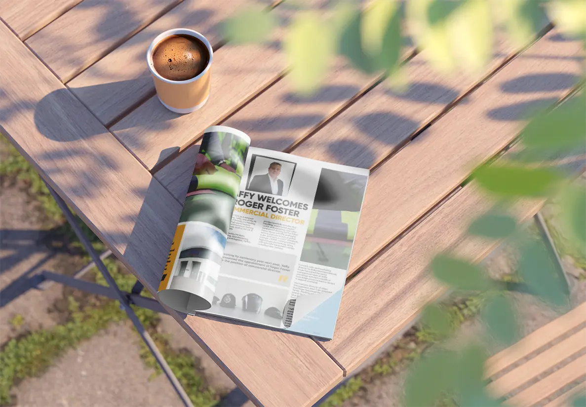 A magazine open on a table next to a coffee. 