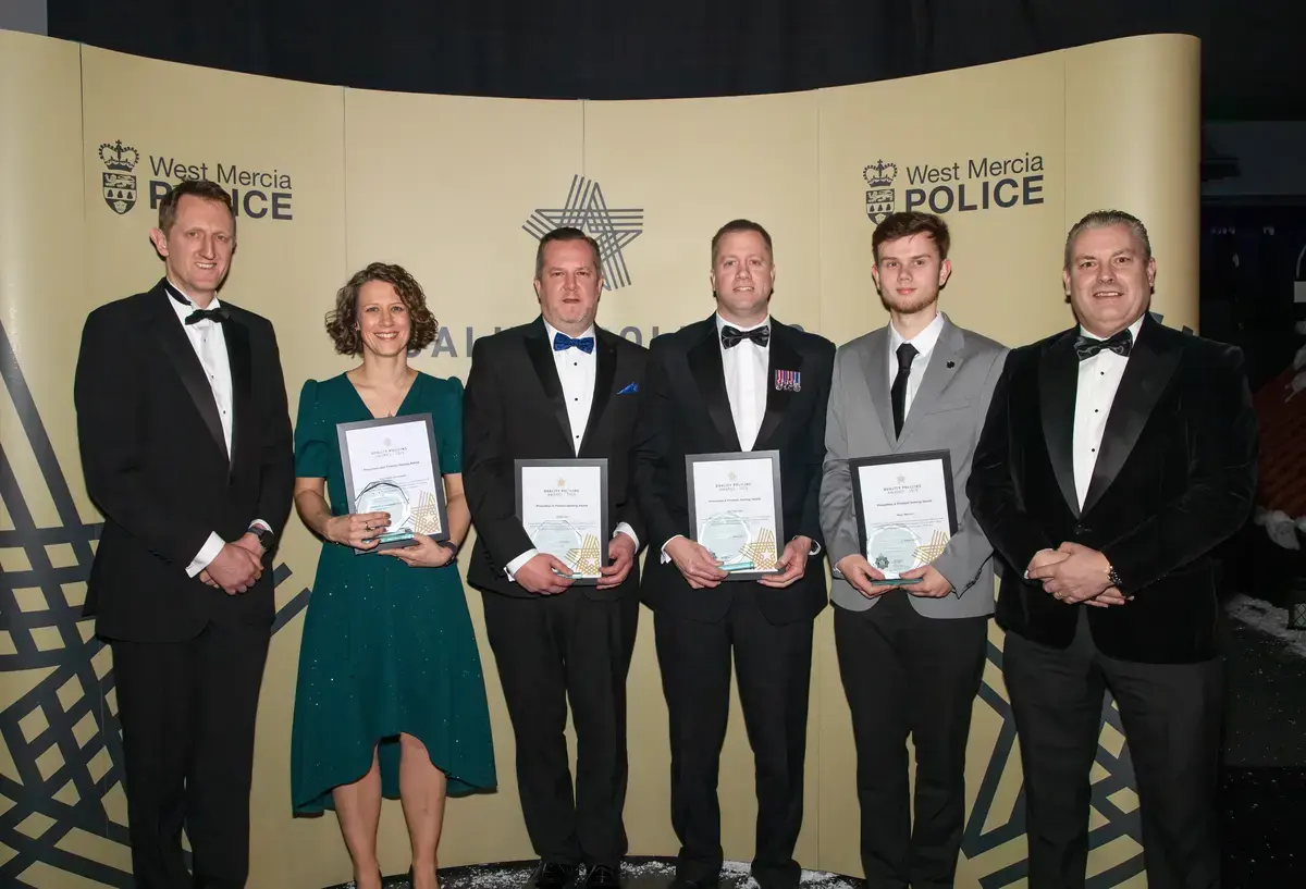 A group of people stood holding certificates dressed in black tie attire. 